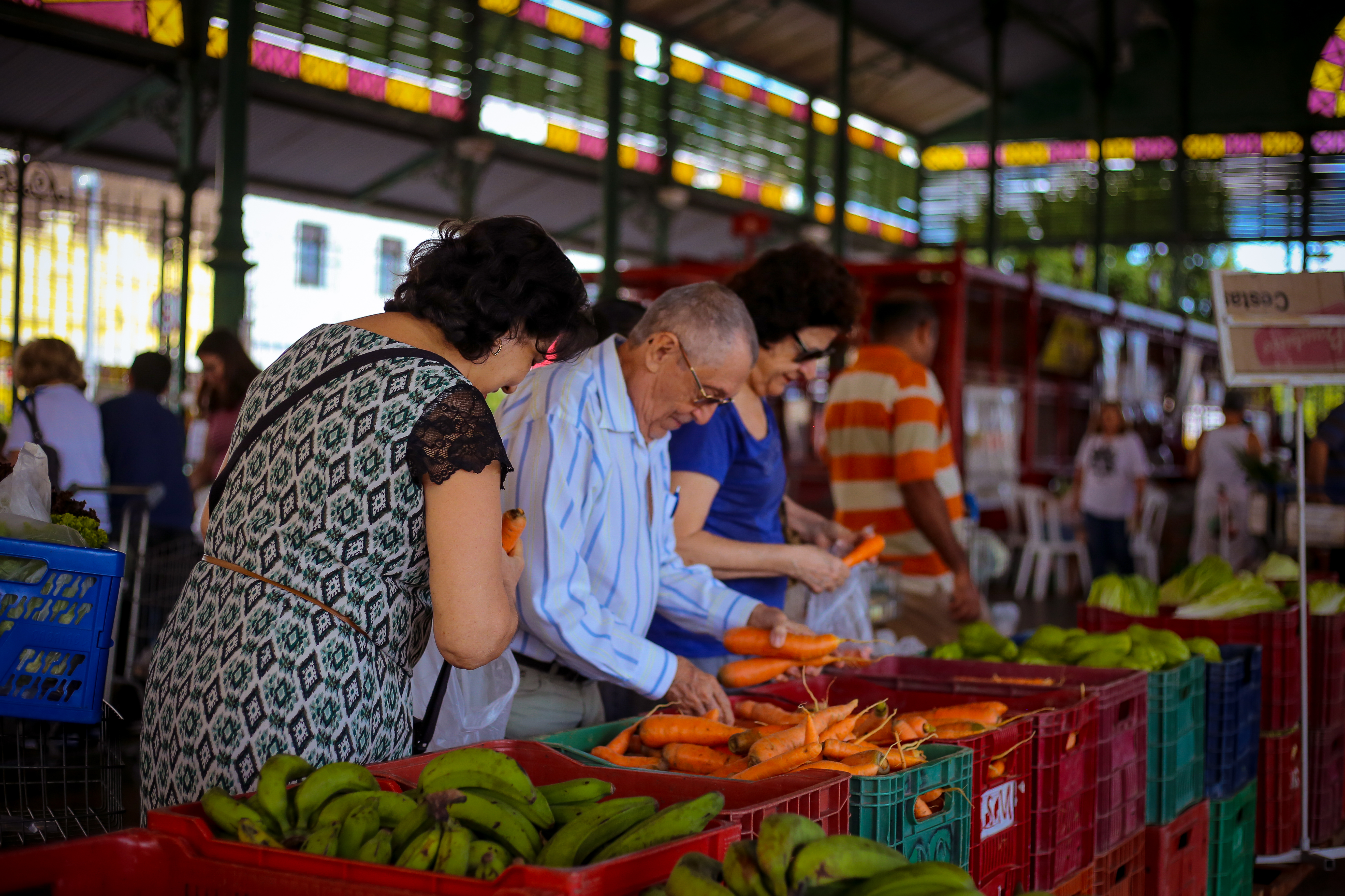 Um senhor e duas senhoras escolhem cenouras e bananas na Feira de Produtos Orgânicos no Mercado dos Pinhões.